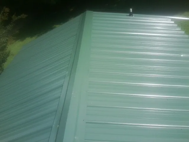 New green metal panels meeting at the ridge of a roof — Flat Roof Repair work by our crew in Mulberry